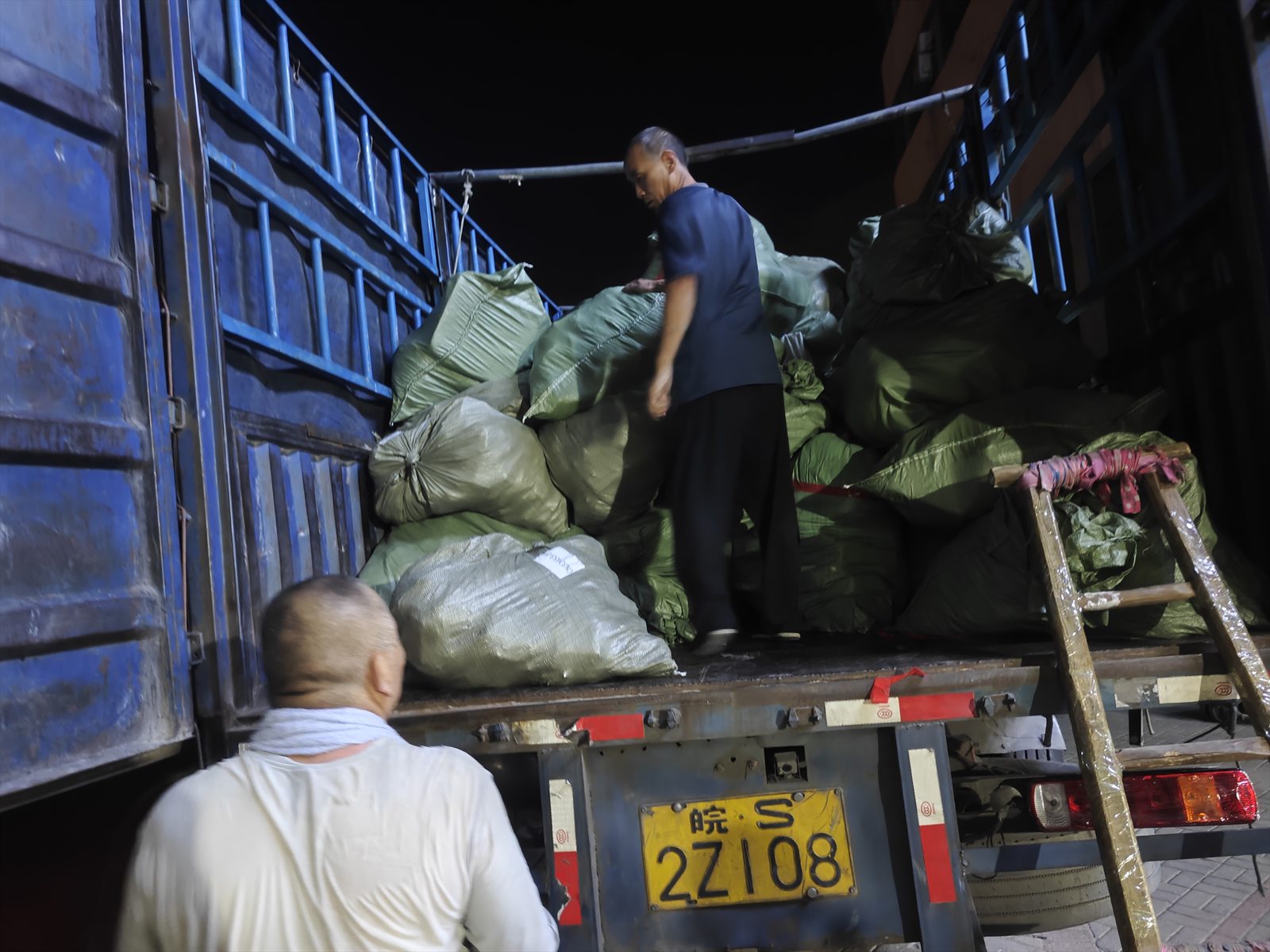 Two members of the DropFulfill operations team loading parcel sacks into a truck at night